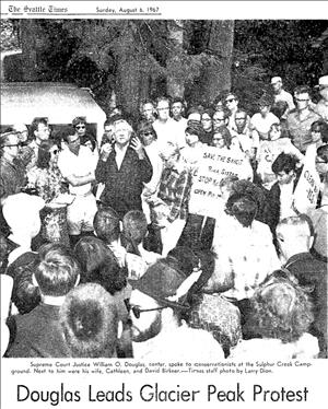 Newspaper clipping shows one man speaking in the middle of a crowd holding signs that say Save the Skagit River